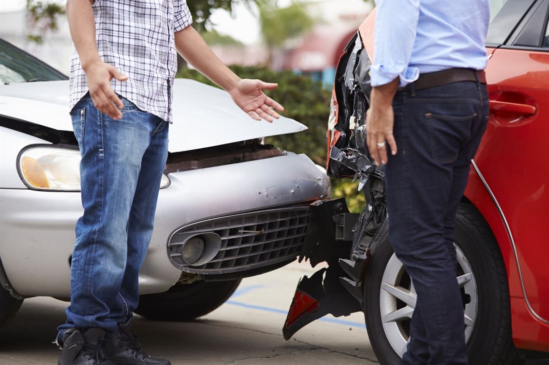 A couple of men standing next to a damaged car

Description automatically generated